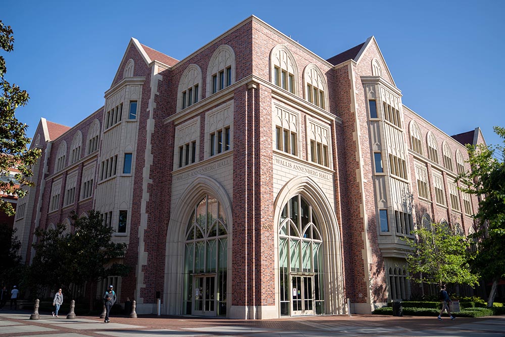南加州大学Wallis Annenberg传播与新闻学院主教学楼外观，拱形玻璃入口与红砖立面设计典雅，学生在楼前行走。